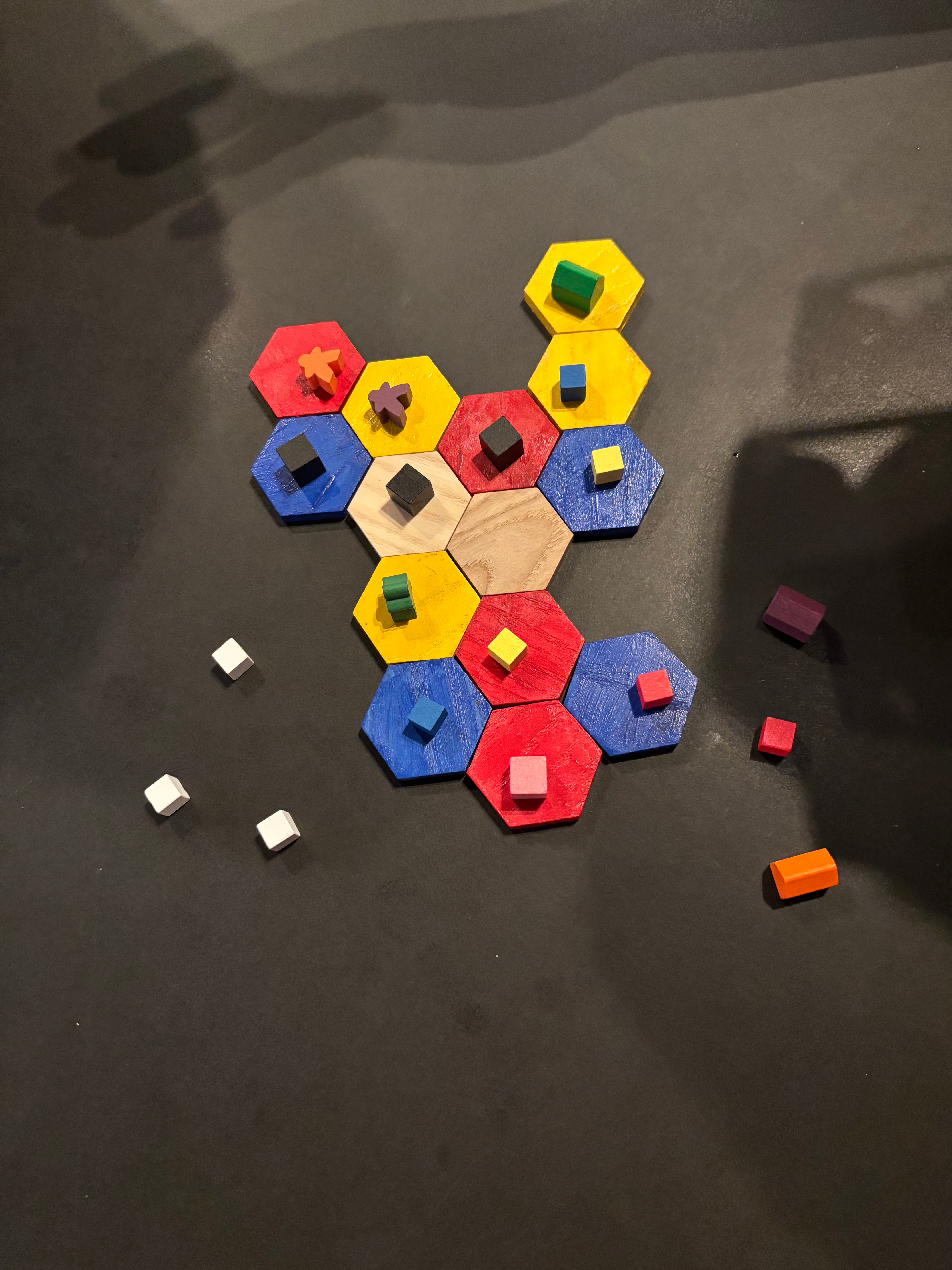 Colored hexes adjoined in a mostly rectangular shape with a scattering of meeple, cubes, and bases -- all pieces are painted wood. 